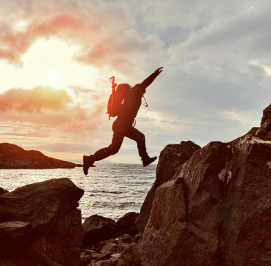 Person jumping between rocks by the ocean at sunset, symbolizing courage and taking a leap forward.