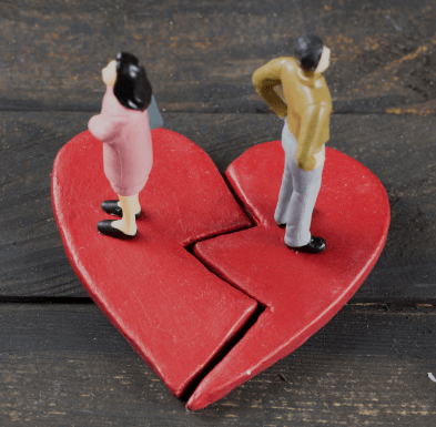 Figurines of a couple standing on a broken heart, symbolizing disillusionment and relationship struggles.