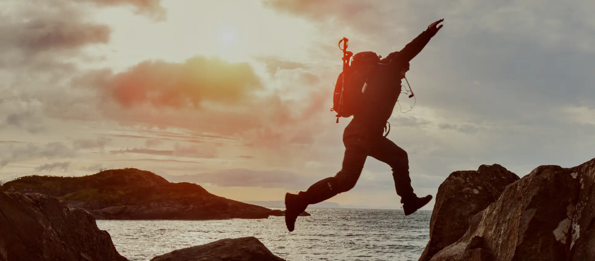 Person jumping between rocks by the ocean at sunset, symbolizing courage and taking a leap forward.