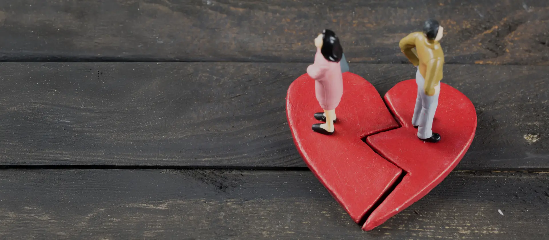 Figurines of a couple standing on a broken heart, symbolizing disillusionment and relationship struggles.