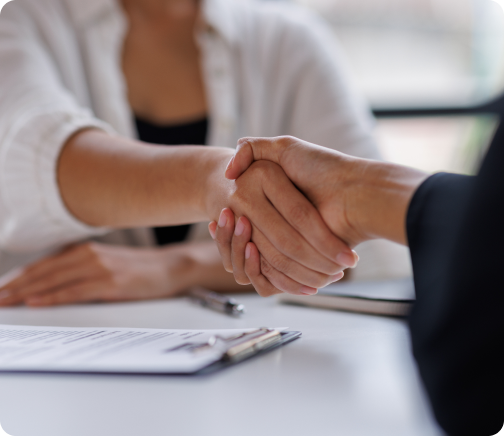 Close-up of two people shaking hands over a desk with documents, symbolizing agreement and collaboration.