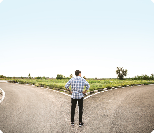 A man stands at a forked road under a clear sky, representing a decision-making moment.